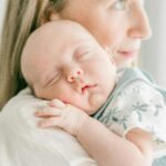 Gros plan d’une mère tenant son bébé endormi, créant une atmosphère sereine et pleine d’amour.