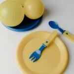 Ensemble de vaisselle pour enfants coloré avec des assiettes jaunes et des couverts bleus, parfait pour des repas ludiques.