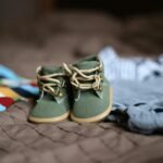 Adorables chaussons pour bébé verts entourés de vêtements colorés, parfaits pour la mode des tout-petits.
