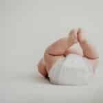 Cute baby lying on back in a diaper against a soft, white background.