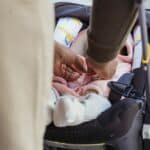 Crop unrecognizable African American father buttoning clothes on infant lying in comfy baby carriage on street