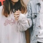 Young couple holding hands in casual attire, symbolizing love and togetherness.